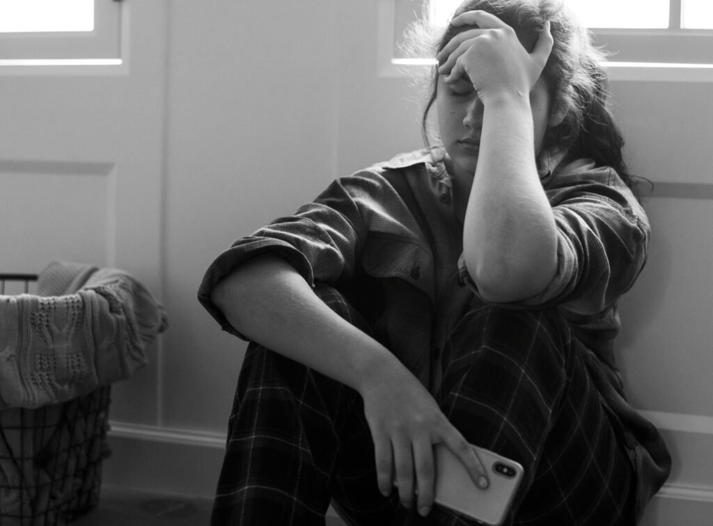 Teenager sitting with head lowered and hand on forehead, appearing withdrawn