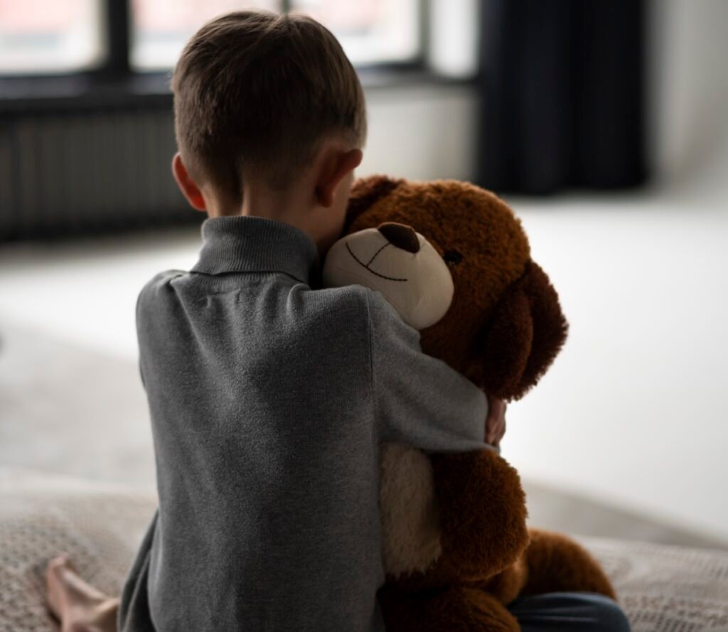 child holding a teddy bear withdrawn and alone