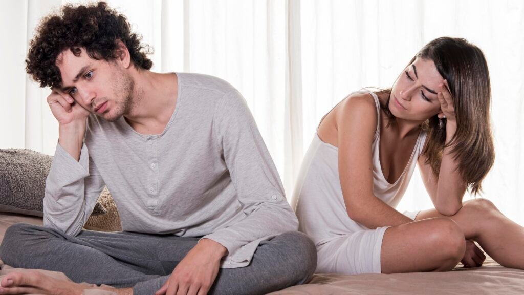 Types of love in relationships: Couple sitting back-to-back on a bed looking upset, showing relationship conflict to depict empty love.