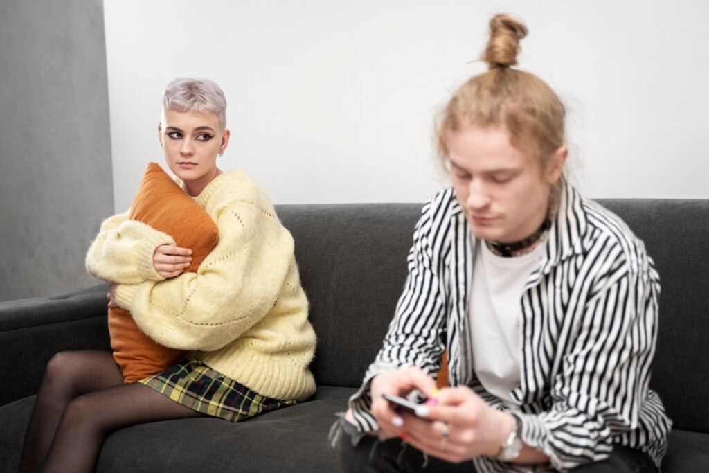 Two young adults sitting apart on a sofa, illustrating social communication differences sometimes experienced by autistic people. 